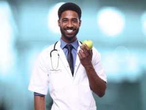 Image shows a smiling doctor holding up an apple
