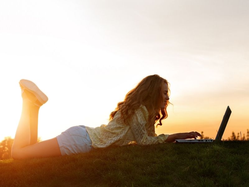 Image of person lying in a field at sunset writing on a laptop