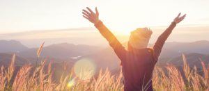 Image of back of person with arms spread looking out at a beautiful mountain scene