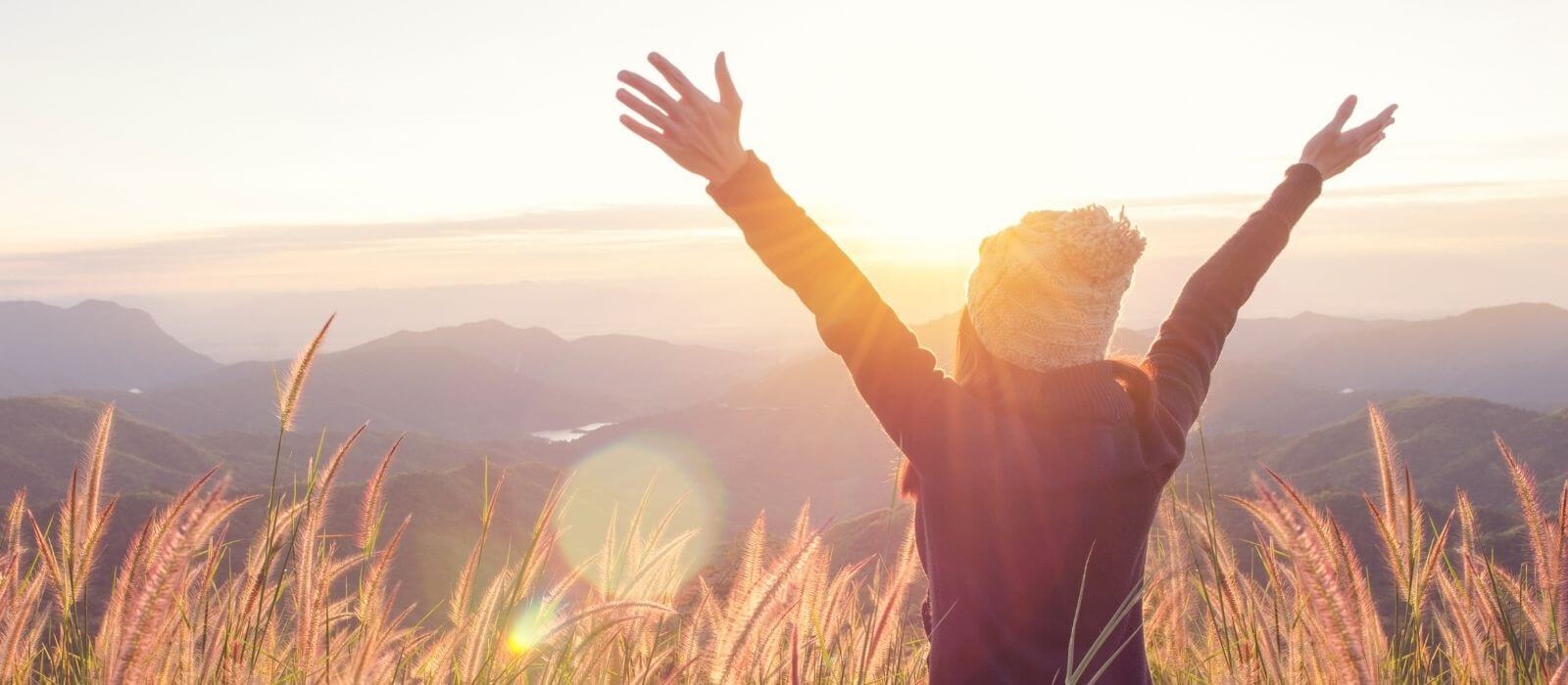 Image of back of person with arms spread looking out at a beautiful mountain scene