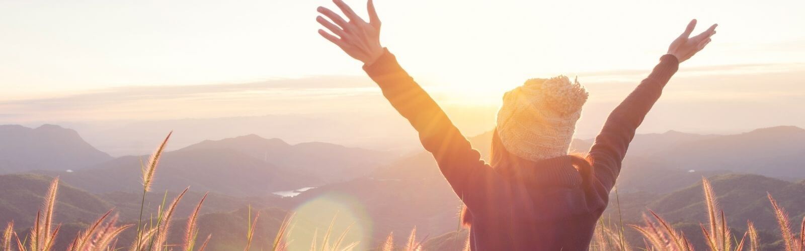 Image of back of person with arms spread looking out at a beautiful mountain scene