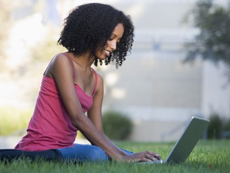 Image of person sitting in grass writing on a laptop