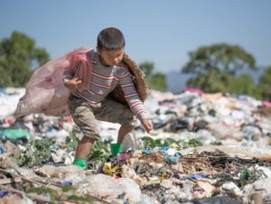 Image shows a child in a landfill picking up trash