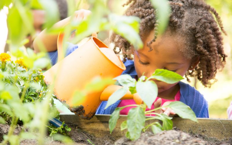A woman holding a basket full of vegetables aA child watering plants in a garden--we need an ethical, sustainable food policy
